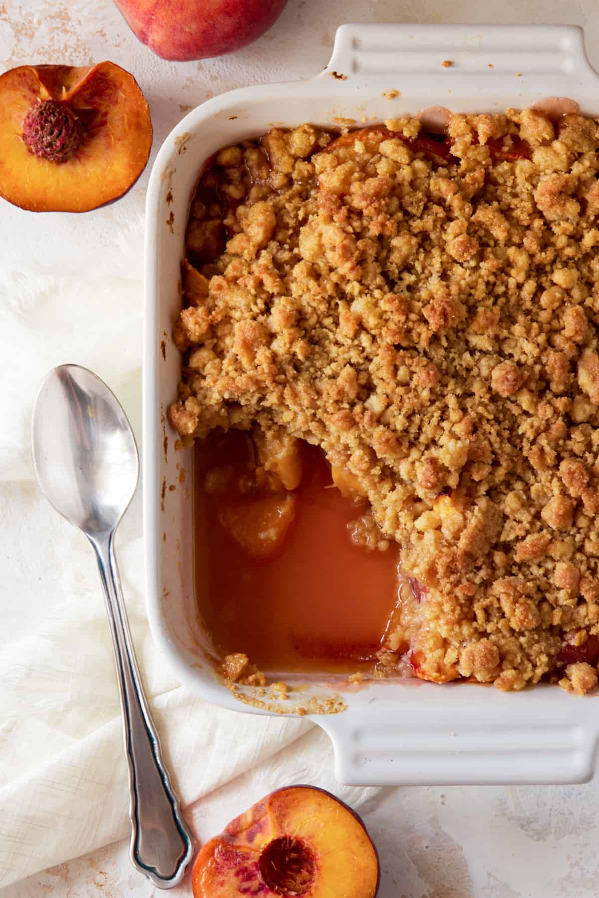 peach crumble in white baking dish with scoop out.