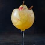 Tall goblet wine glass filled with apple cider sangria, ice and apple slices.