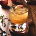 Apple cider and bourbon cocktail in lowball glass with fresh apple slices and thyme sprigs.