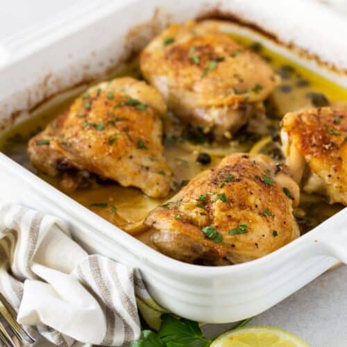 Four baked chicken thighs in white casserole dish.