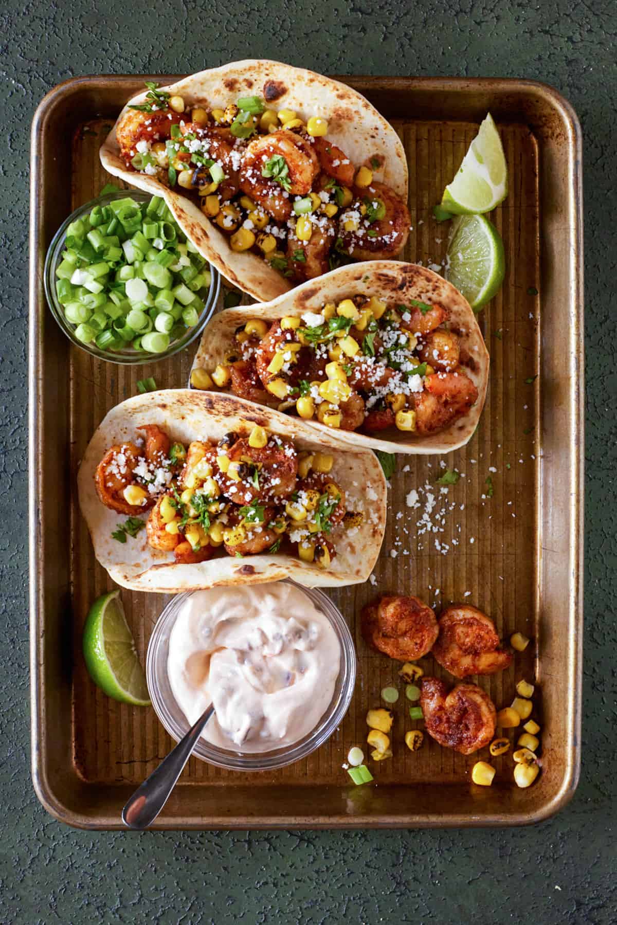 Baking tray with three tacos, corn and chipotle cream.