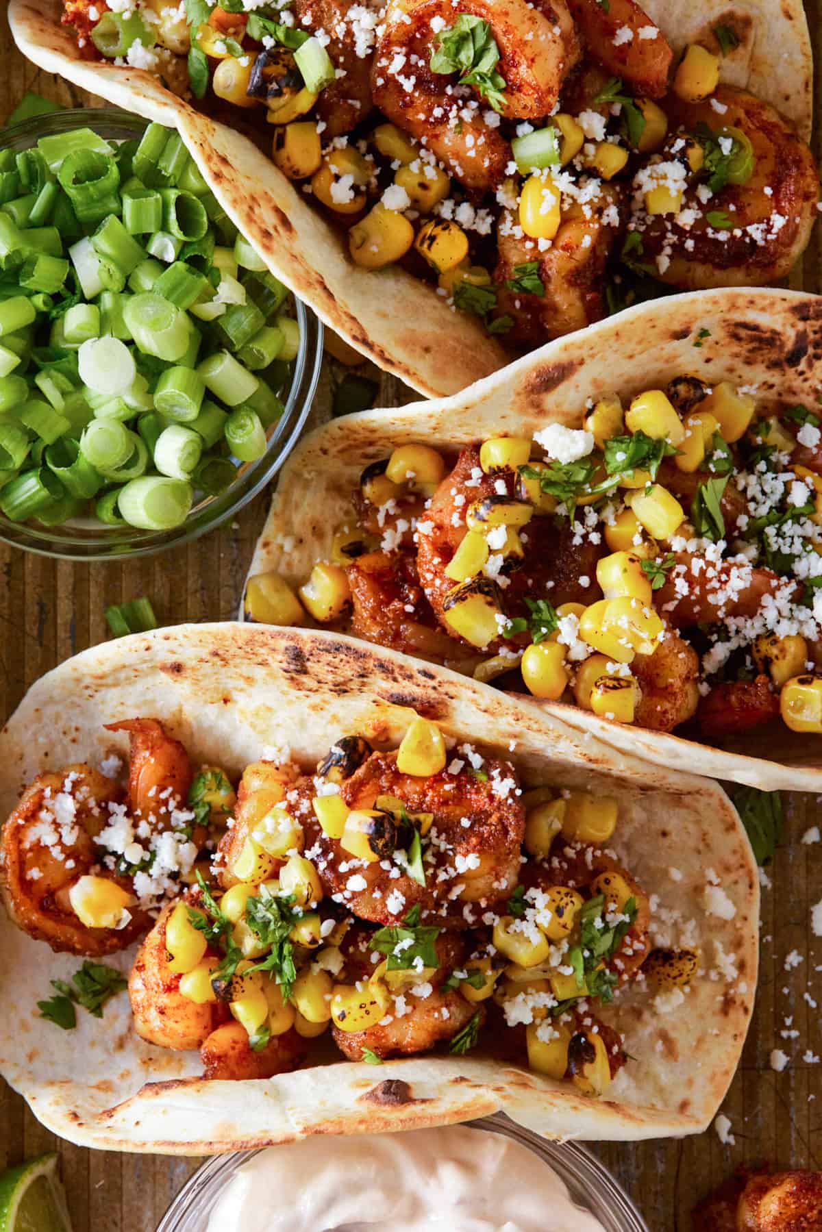 Shrimp tacos on baking sheet with green onions and lime wedges.