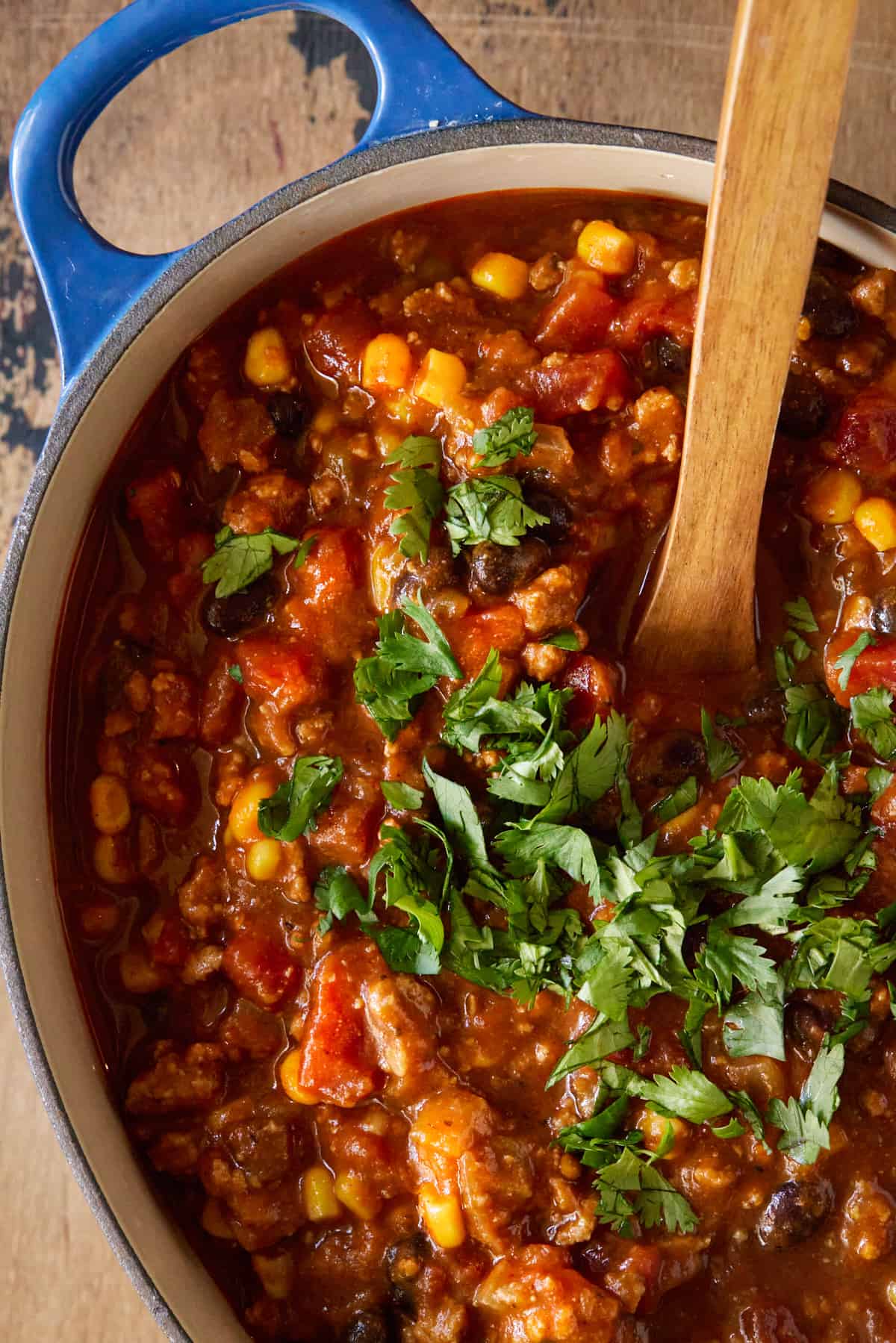 Chili in dutch oven with wooden spoon and chopped cilantro.