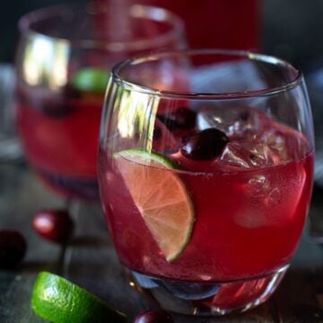 Glass of cranberry vodka punch with ice and lime wedges.