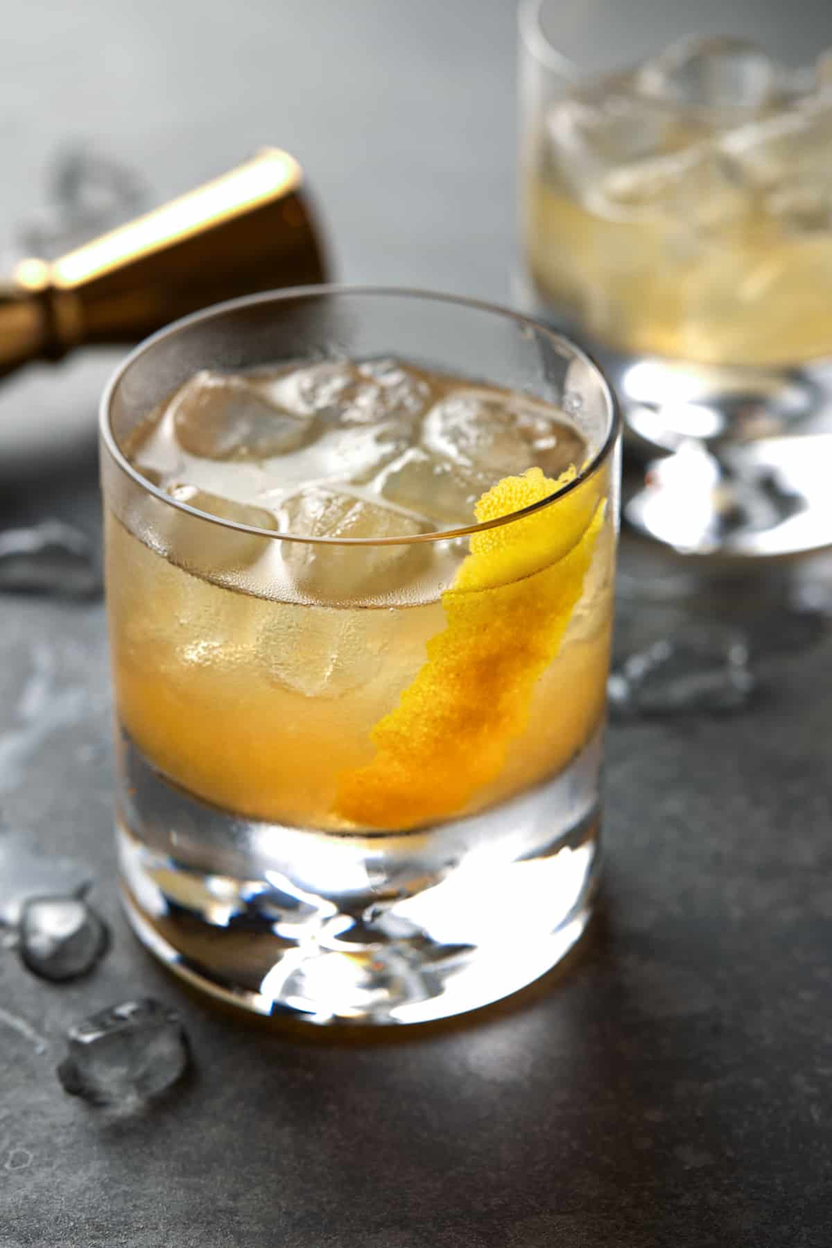 Lowball glass of golden cocktail on a dark gray board. 