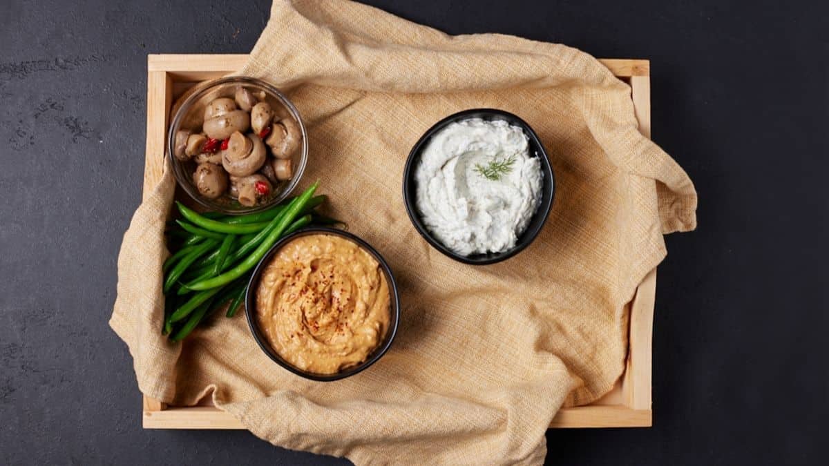 Wooden tray with bowls of dip and veggies. 