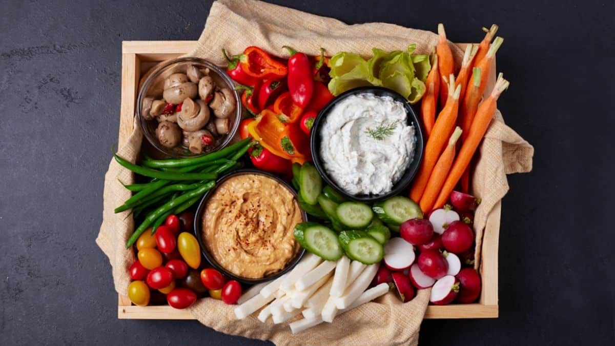 Veggies in a wooden tray with bowls of dip. 