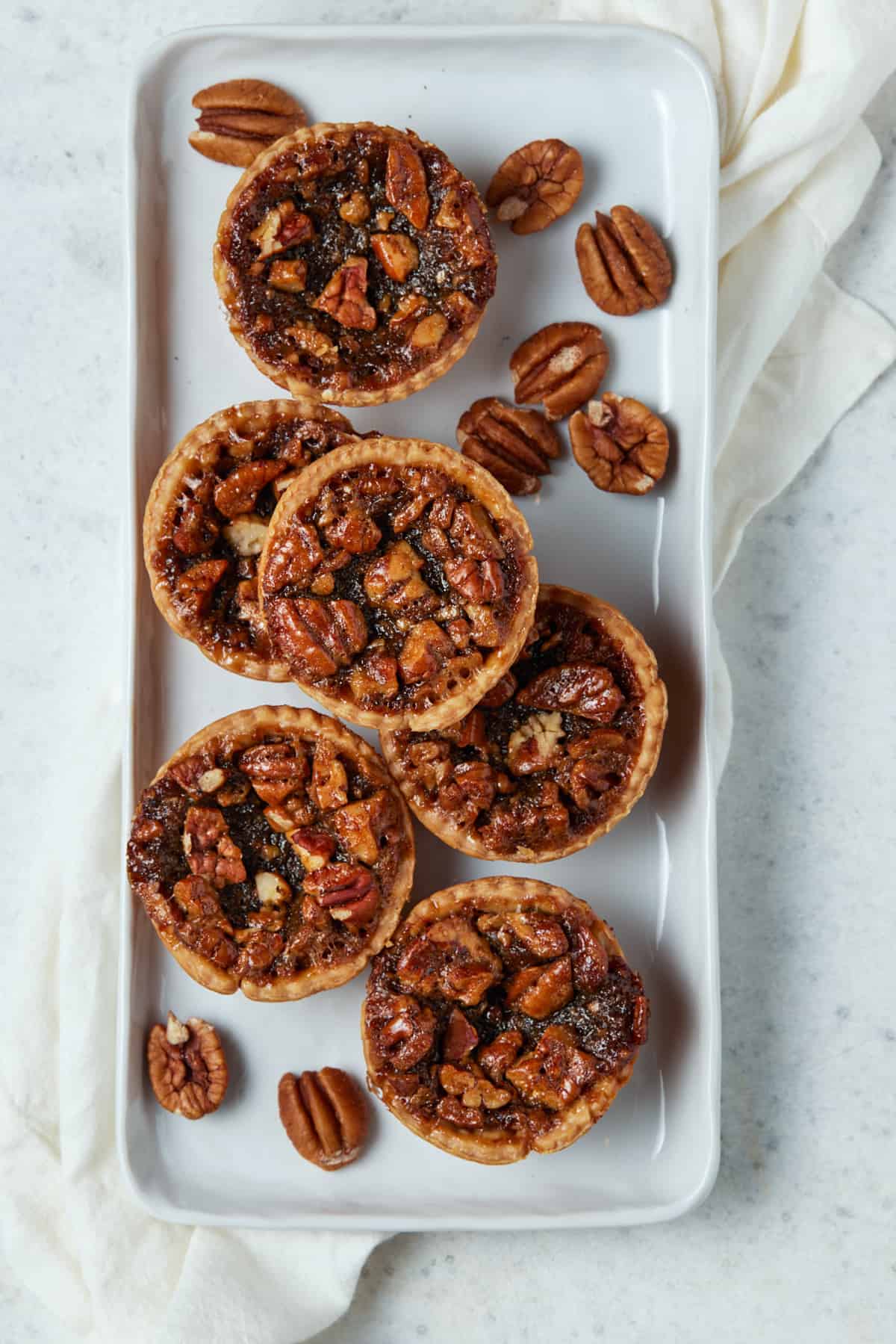 Mini Pecan Pies on white tray with pecans.