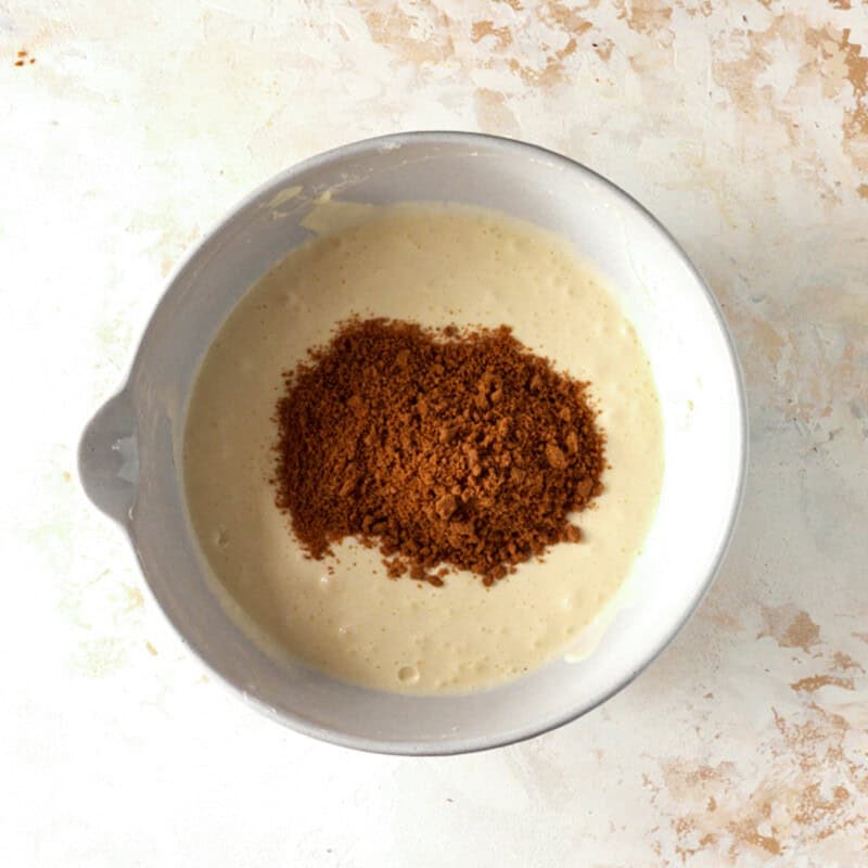 Biscoff cookie crumbs on top of cheesecake batter in a white mixing bowl.