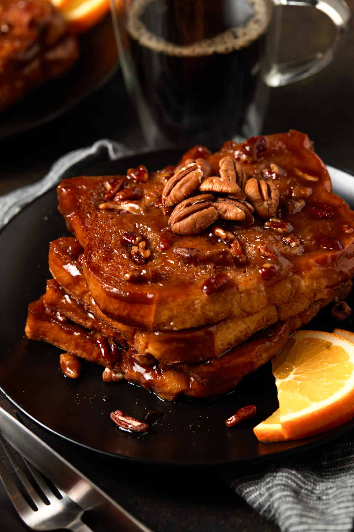 Slices of caramel pecan brioche french toast on a black plate with an orange slice. 