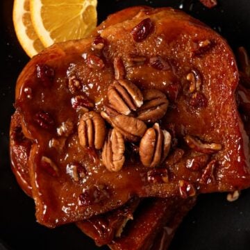 Pieces of brioche french toast on a black plate. Topped with pecans.