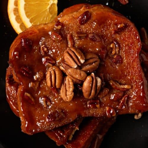 Pieces of brioche french toast on a black plate. Topped with pecans.