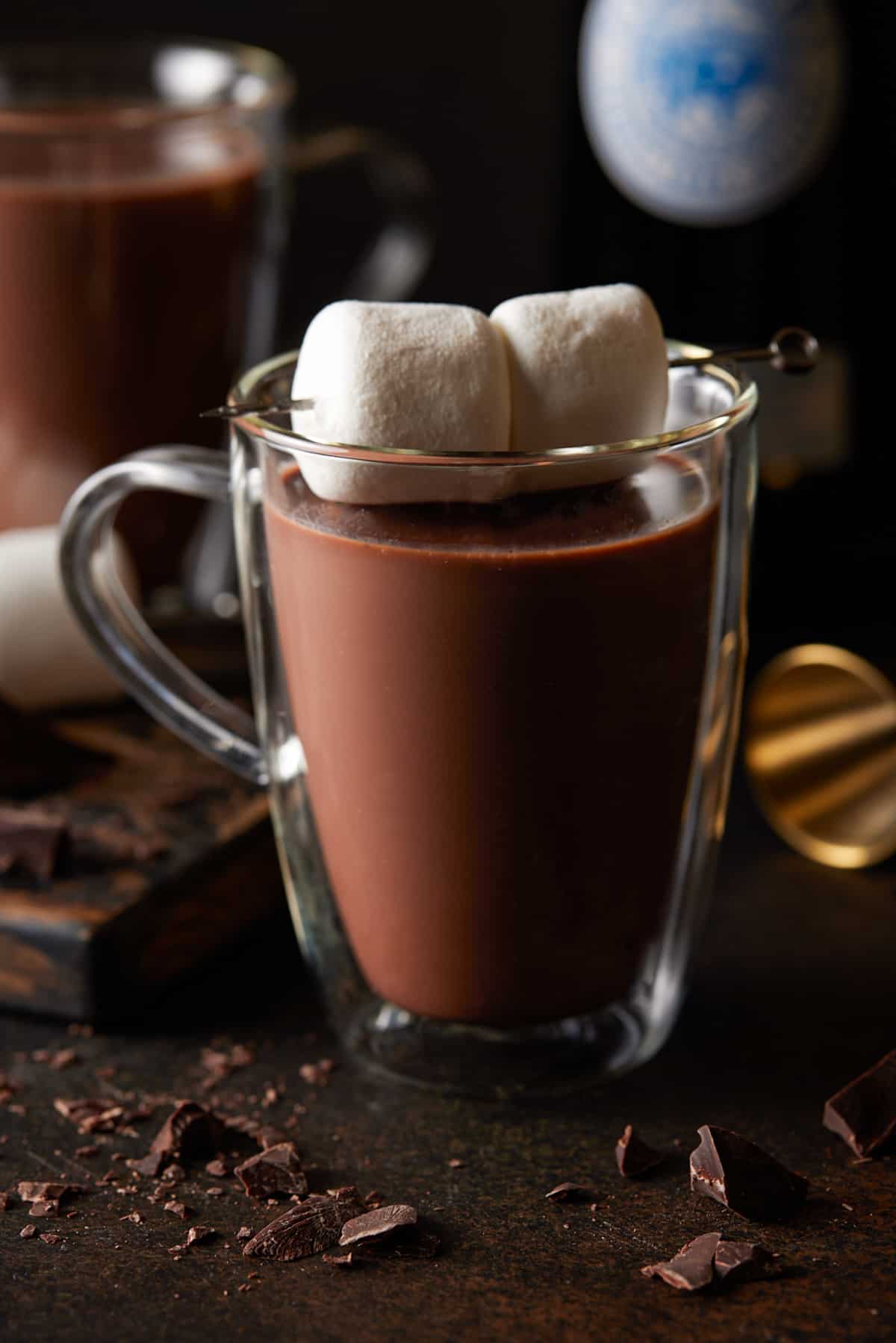 Glass mug of spiked hot chocolate garnished with a skewer of two large marshmallows. 