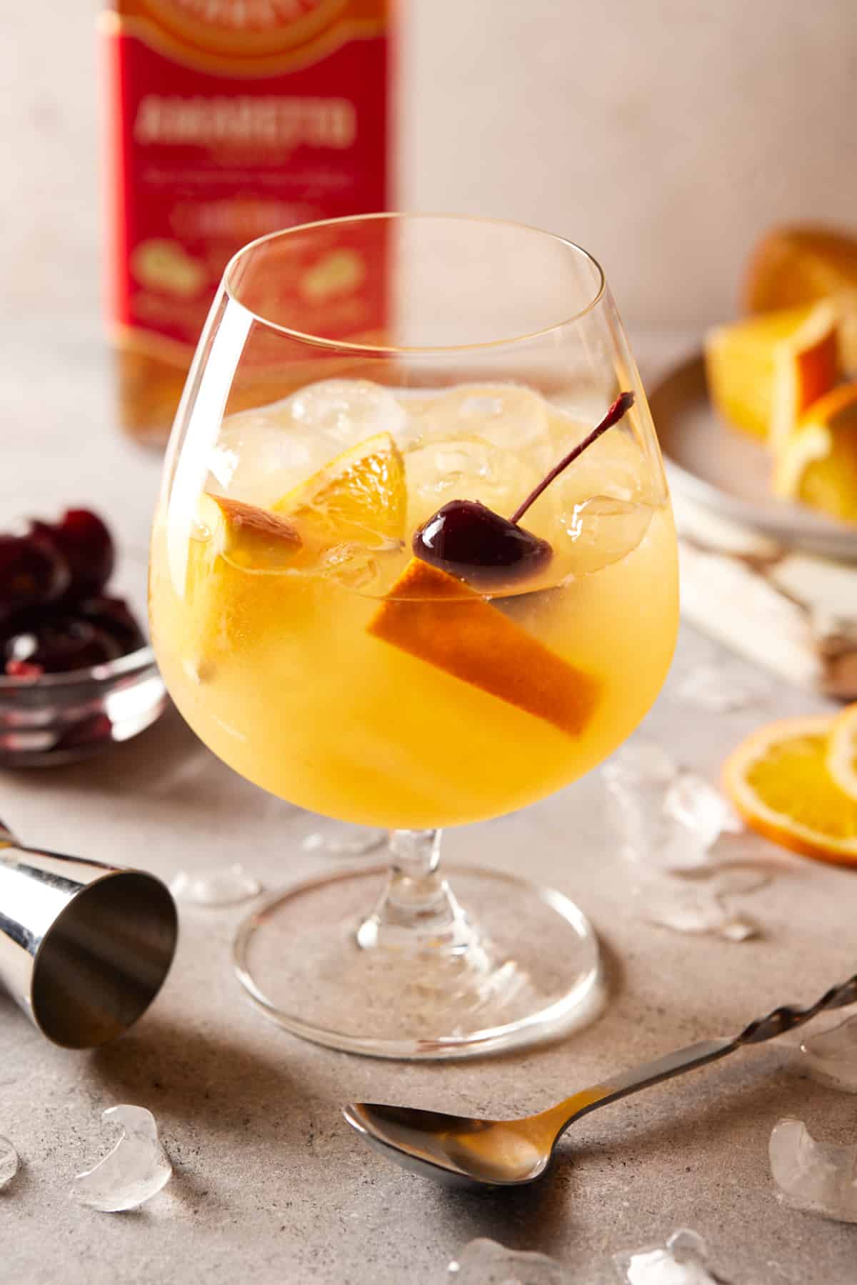 Orange juice brunch cocktail in a footed glass garnished with cocktail cherries and orange slices.