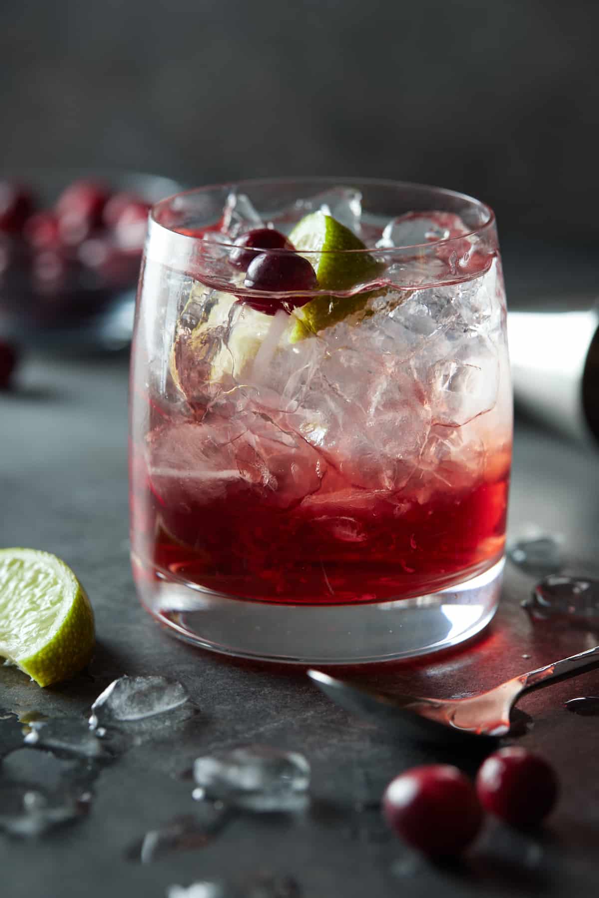 Low ball glass filled with drink with cranberries and lime wedges.