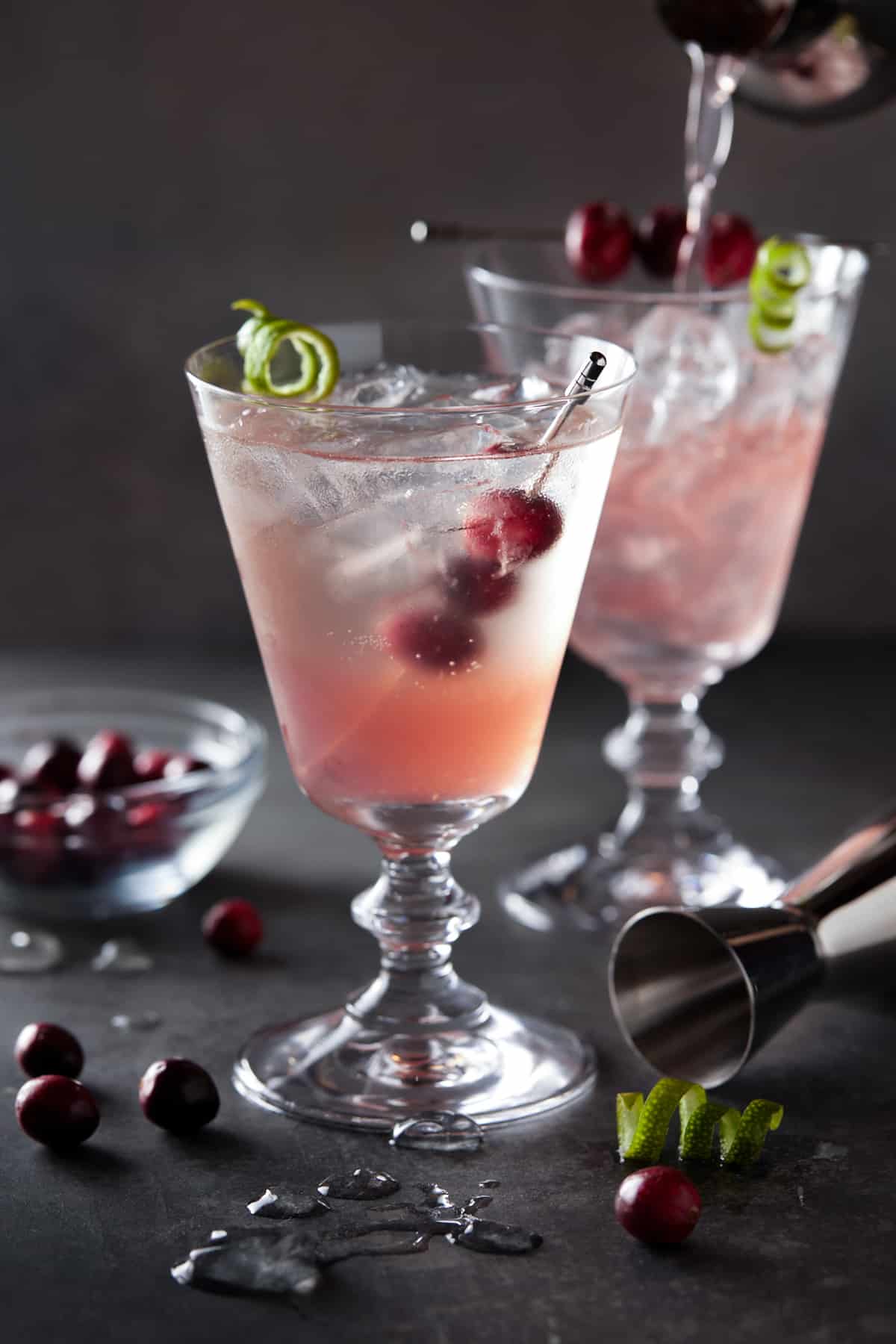 Ice filled glasses with cranberry gin cocktail. Garnished with fresh cranberries and a lime twist. 