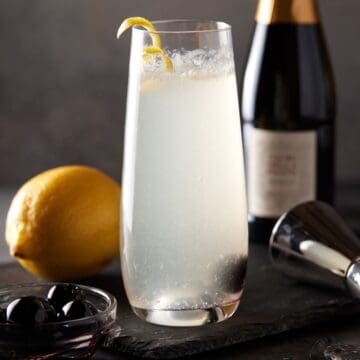 Filled champagne flute with lemon twist and cherry.