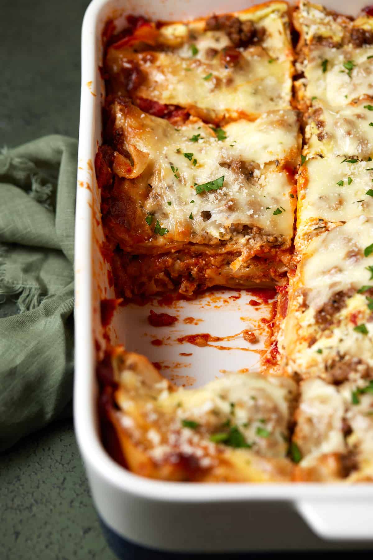 White casserole dish of lasagna with piece cut out.