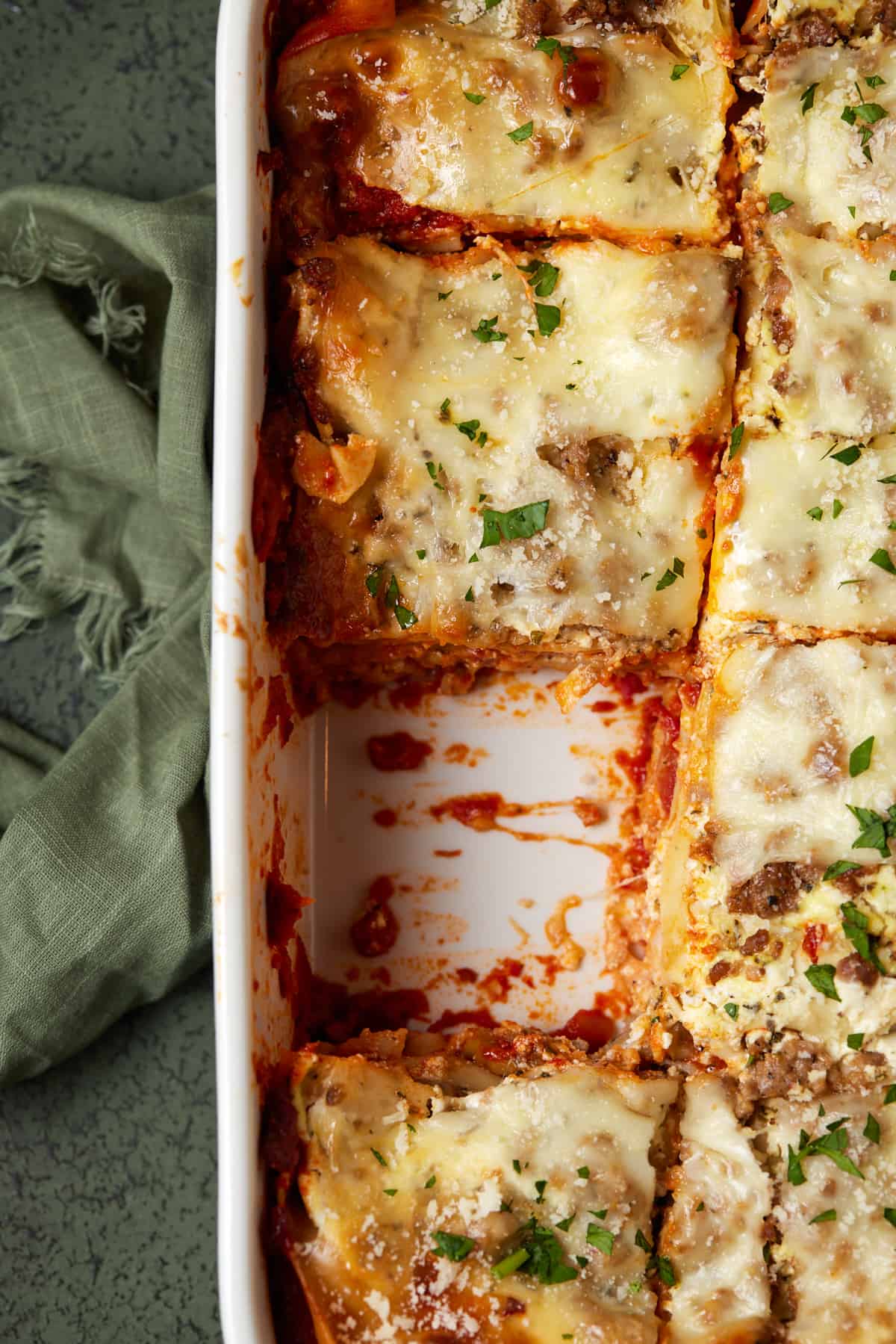 Lasagna in white casserole dish with one piece missing. 