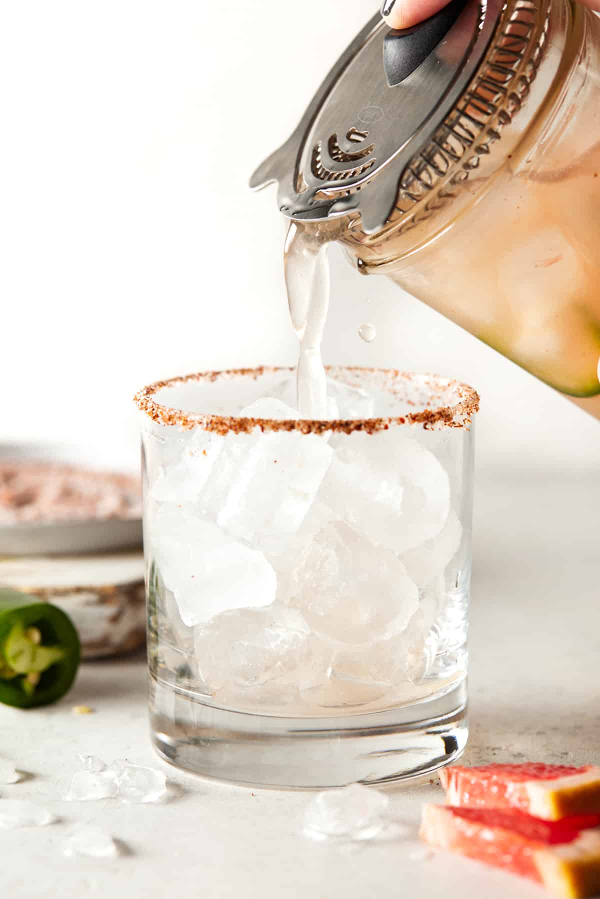 Hand pouring grapefruit margarita into lowball glass filled with ice. 