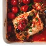 Baked fish fillet with tomatoes in a white casserole dish.