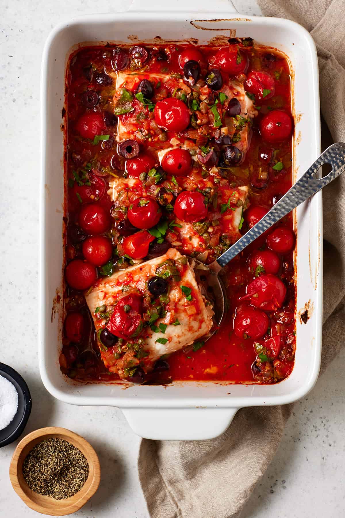 Baked mahi mahi fillets with tomatoes and olives in white casserole dish. 