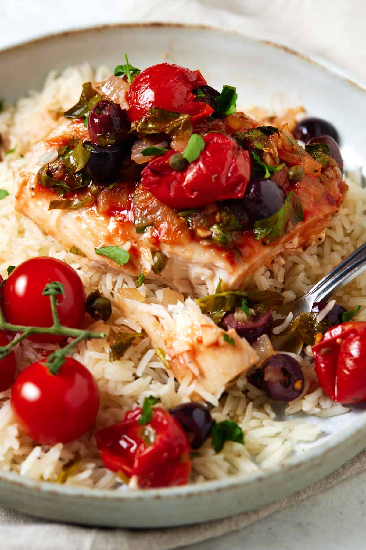 Baked mahi mahi with tomato olive sauce served over rice in a bowl. 