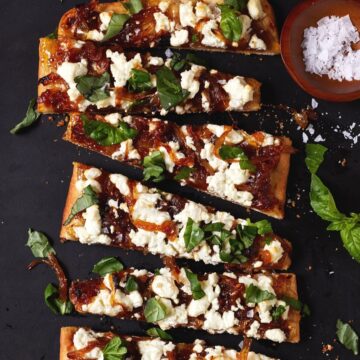 Pieces of goat cheese pizza on black cutting board.