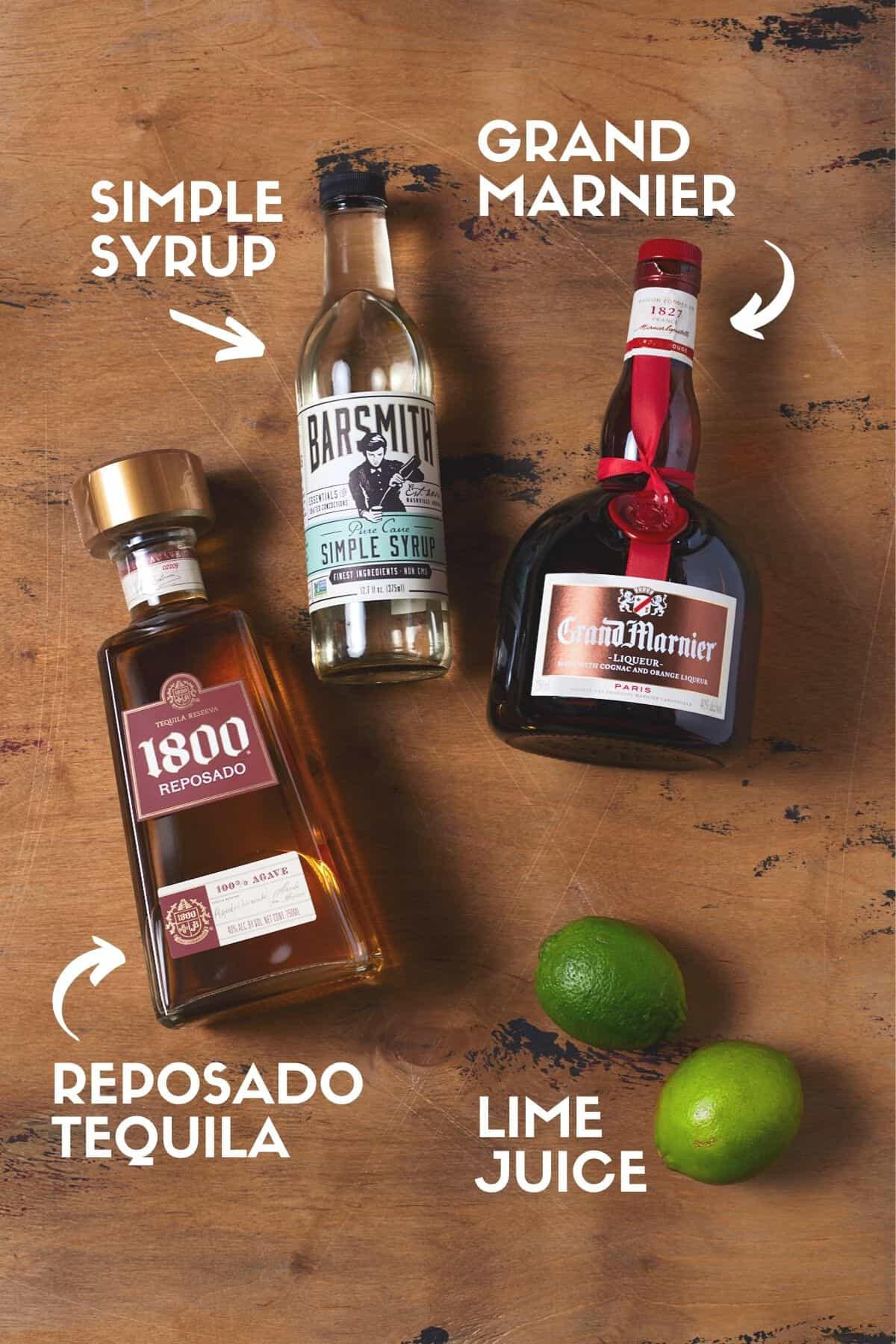 Bottles of tequila, simple syrup, grand marnier and fresh limes on a wood board. 