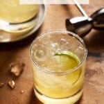 two golden margaritas on a brown board with ice chips.