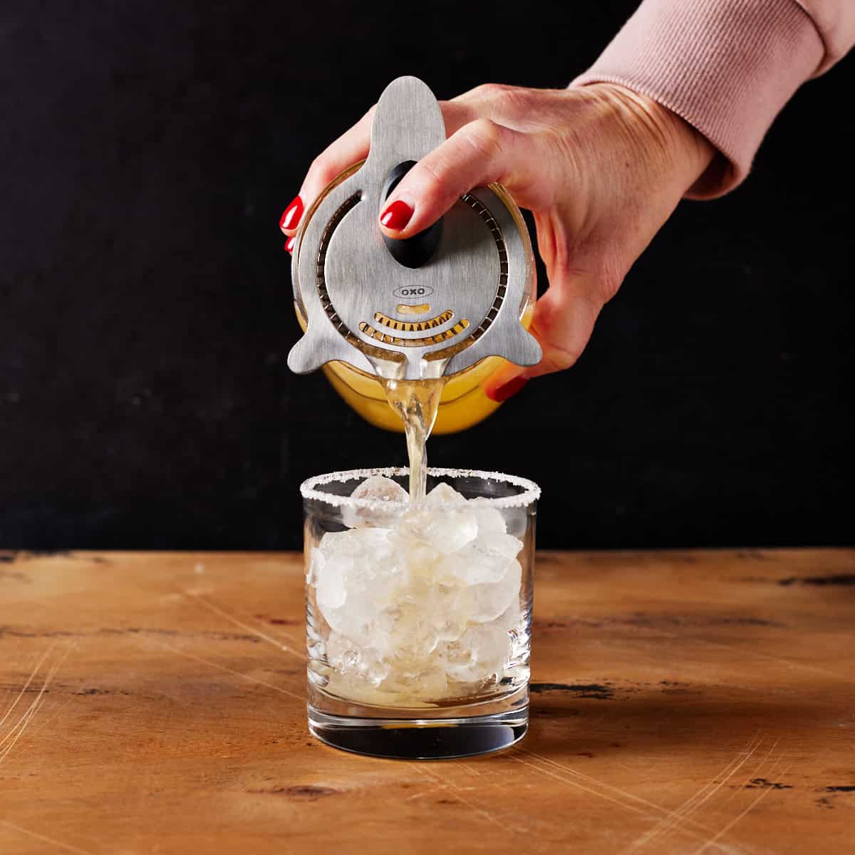 shkaer pouring drink into ice filled salt rimmed glass.