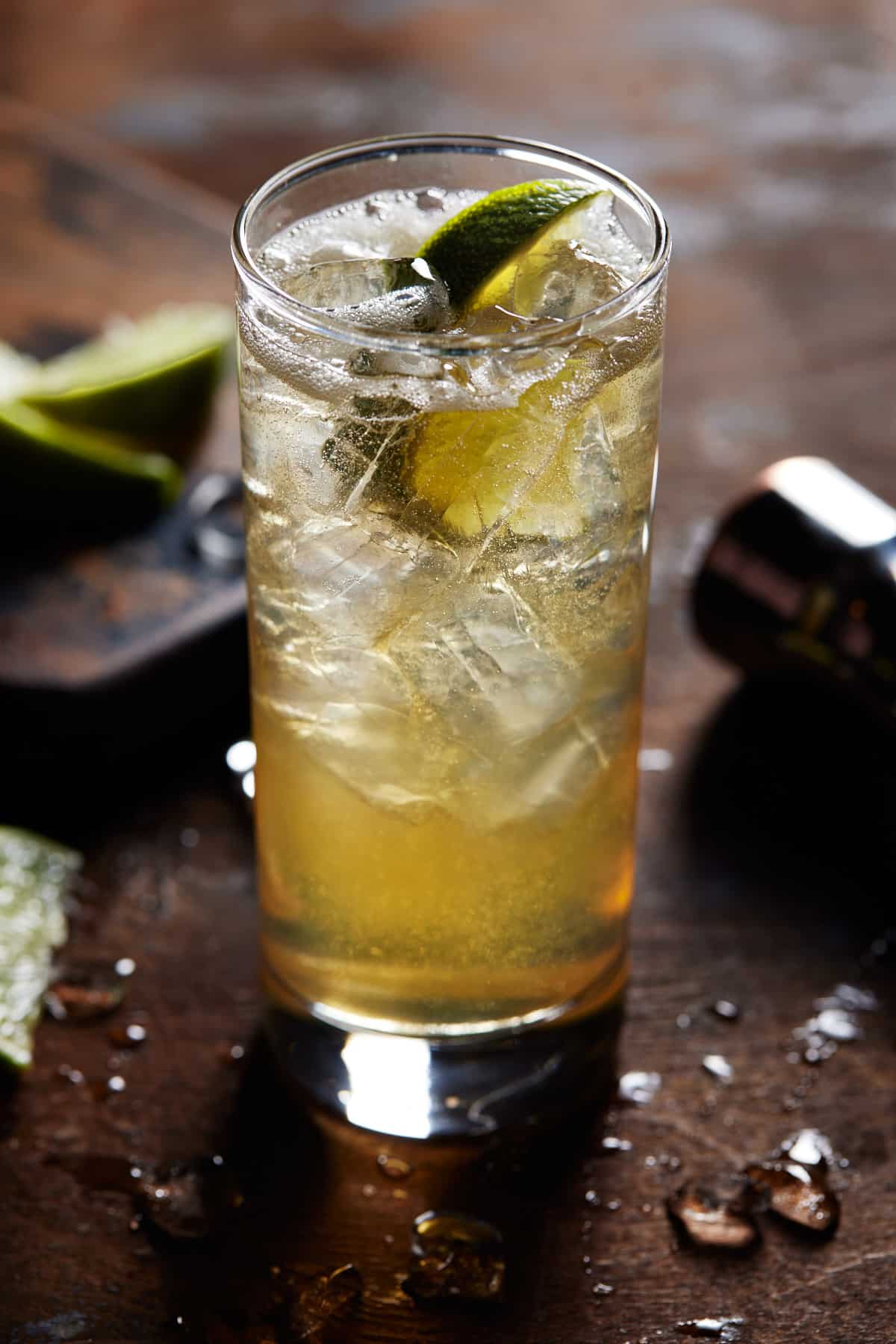 Whiskey Ginger Cocktail in a highball glass with ice and a lime wedge. 