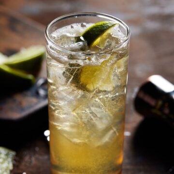 Highball glass of whiskey ginger cocktail with lime wedge.