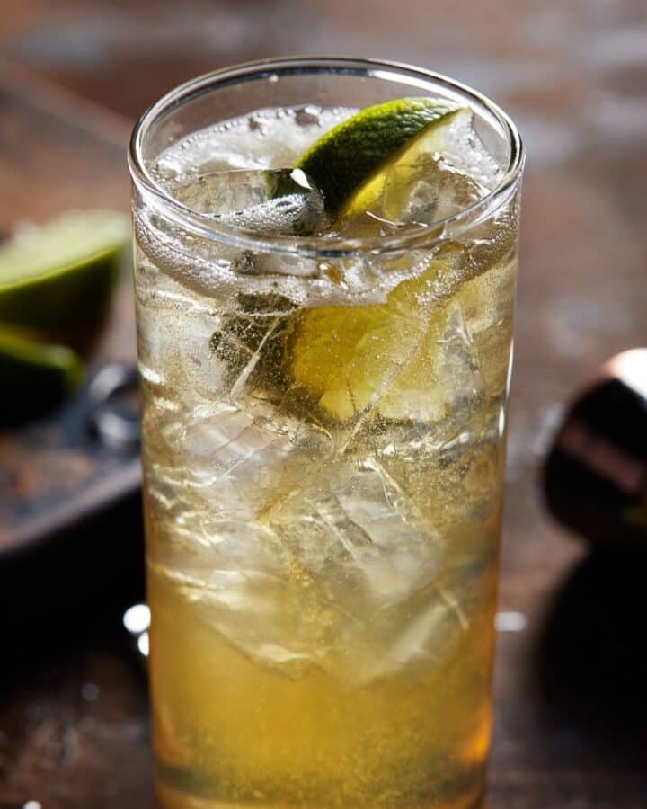 Highball glass of whiskey ginger cocktail with lime wedge.