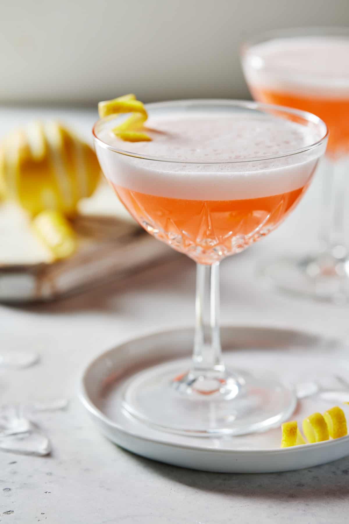 Coupe glass filled with Aperol Sour with lemon twist.