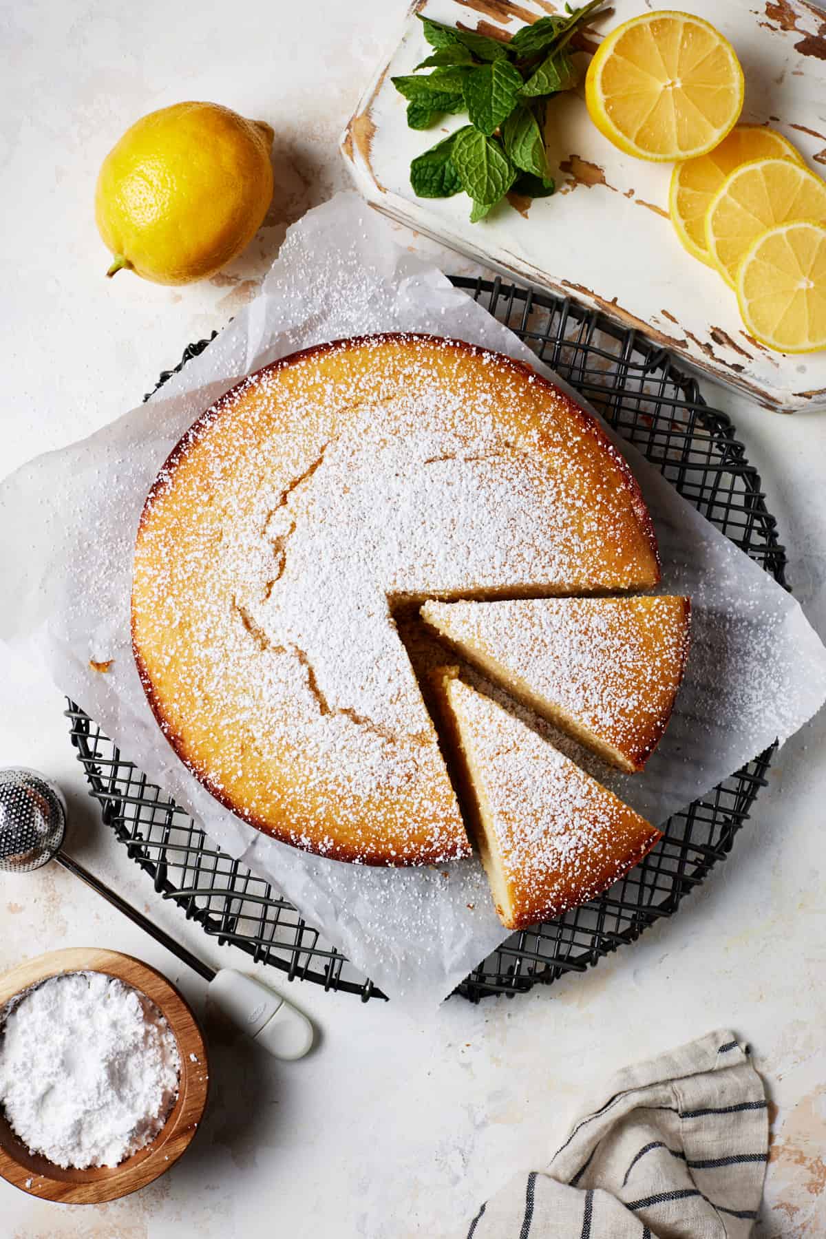 Lemon Ricotta Cake on a dark cooling rack with slices removed. Sprinkled with powdered sugar. 