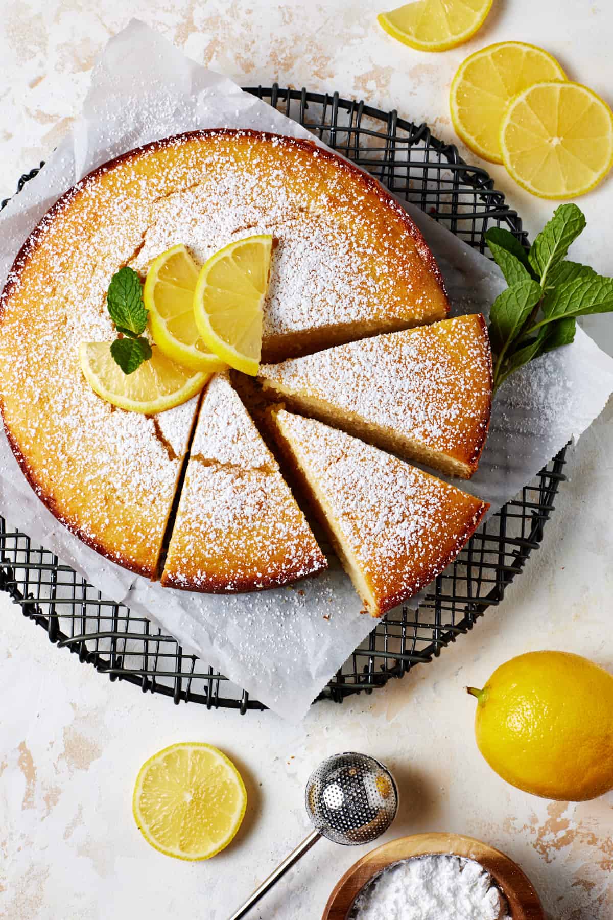 Whole lemon ricotta cake sprinkled with powdered sugar and garnished with lemon slices and fresh mint. 