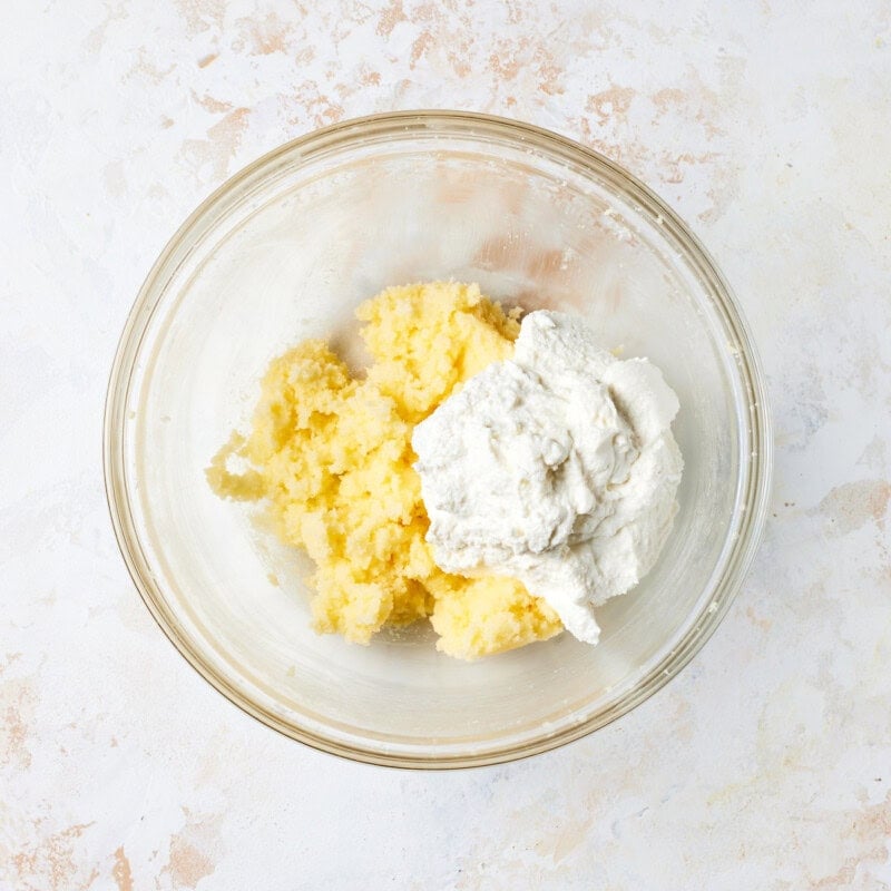 Ricotta cheese added to creamed butter and sugar mixture in glass bowl. 