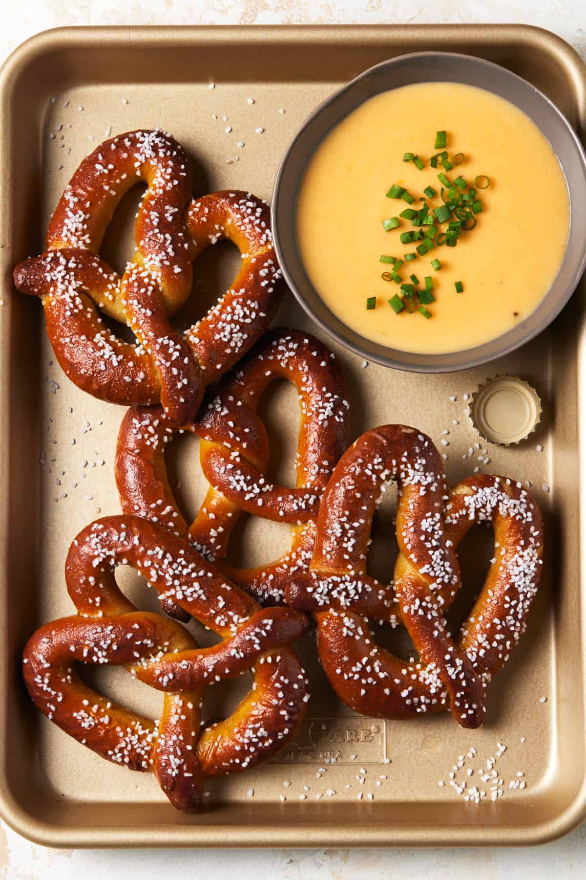 Bowl of cheese dip and soft baked pretzels with salt on tray.