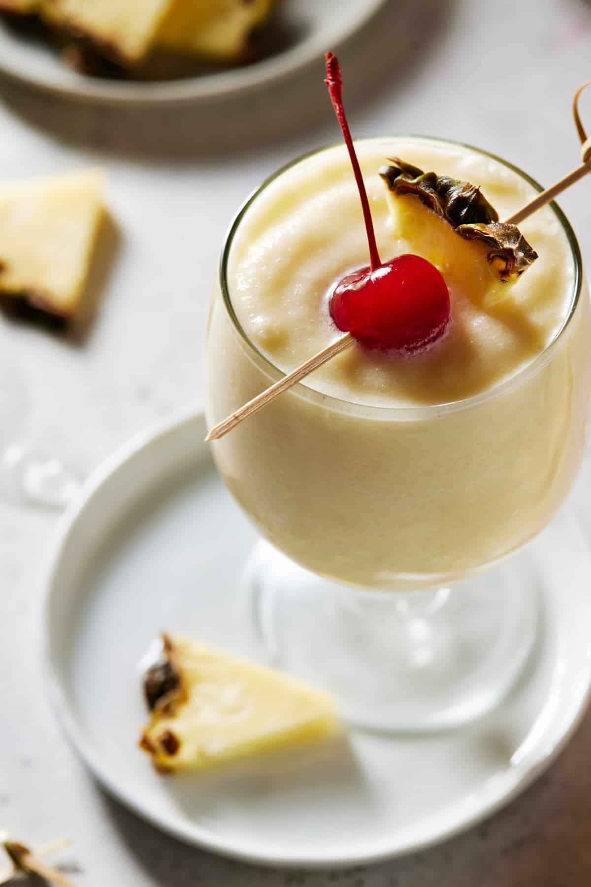 Footed glass of virgin piña colada with a pineapple wedge and maraschino cherry. 