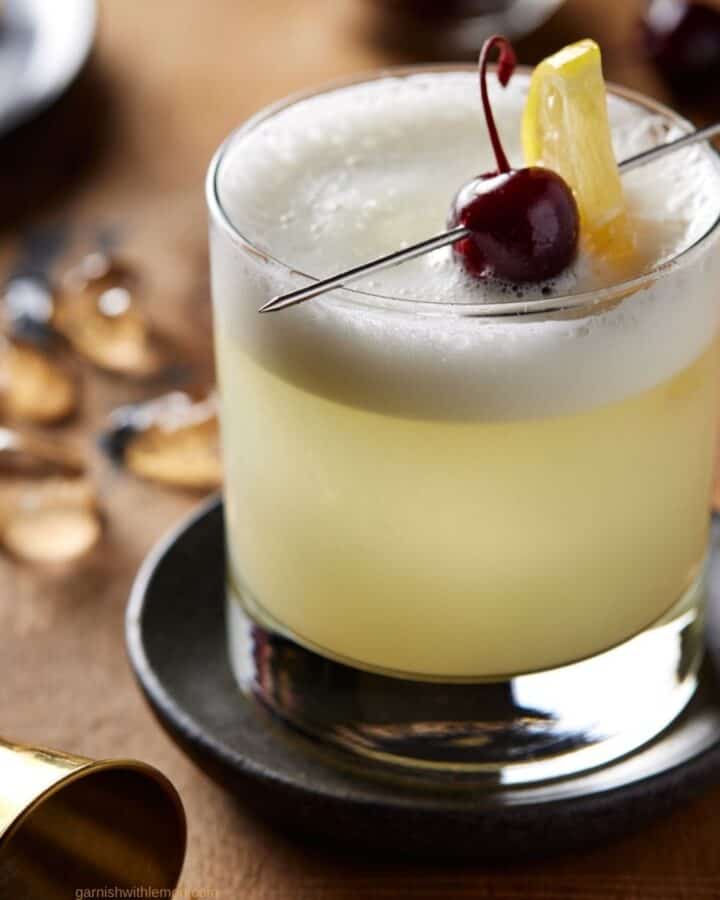 vodka sour in a low ball glass with a lemon slice and cherry.