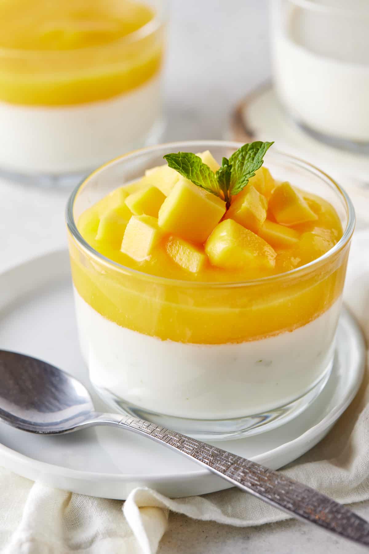 Single glass ramekin filled with mango panna cotta and garnished with mint leaf. 