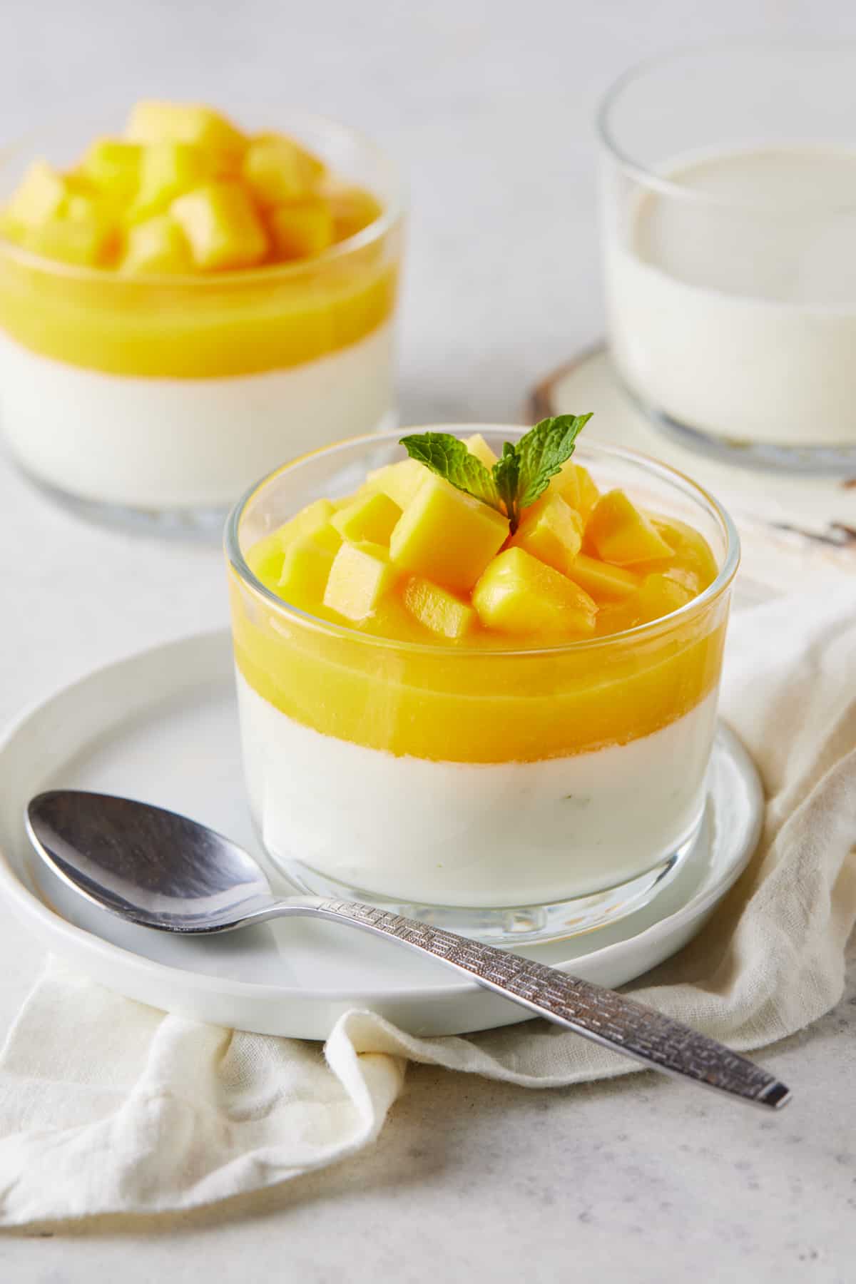 Clear ramekins filled with mango panna cotta on white plates. 