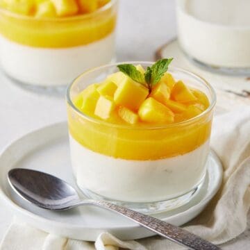 Clear ramekin filled with mango panna cotta on a white plate.