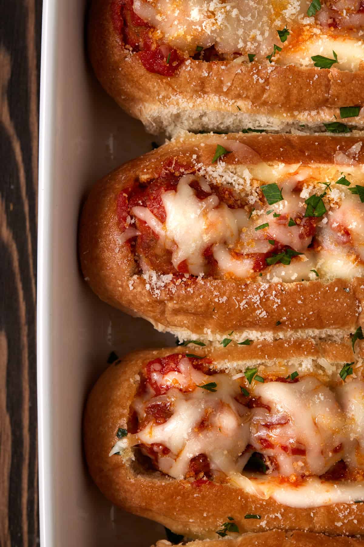 Toasted meatball subs in a white casserole dish. 