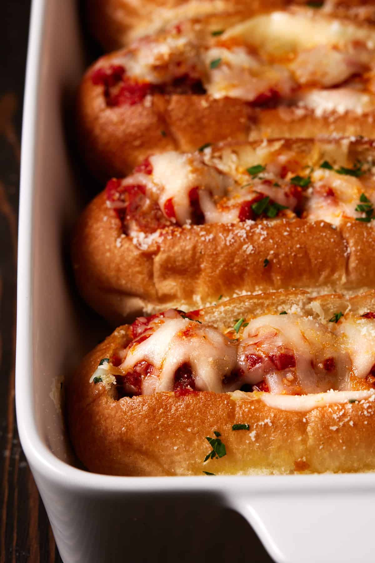 Baked meatball subs with melted cheese in white casserole dish. 