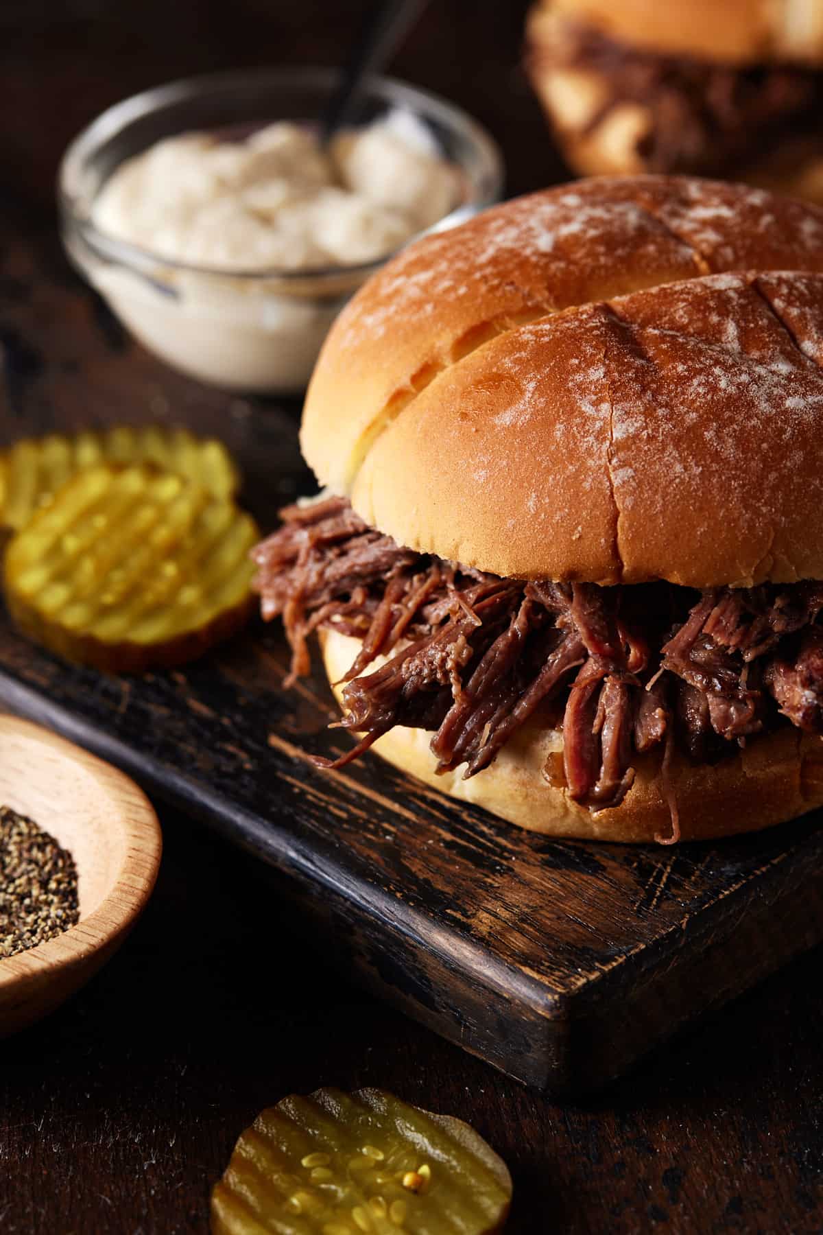 Pulled beef sandwich on cutting board with pickles.