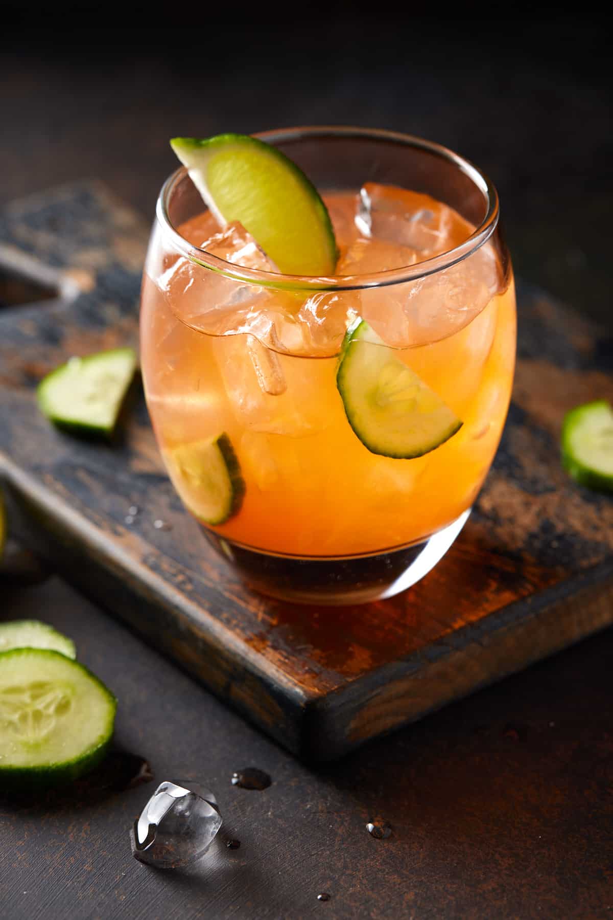 Low ball glass filled with ice, orange drink and cucumber slices.