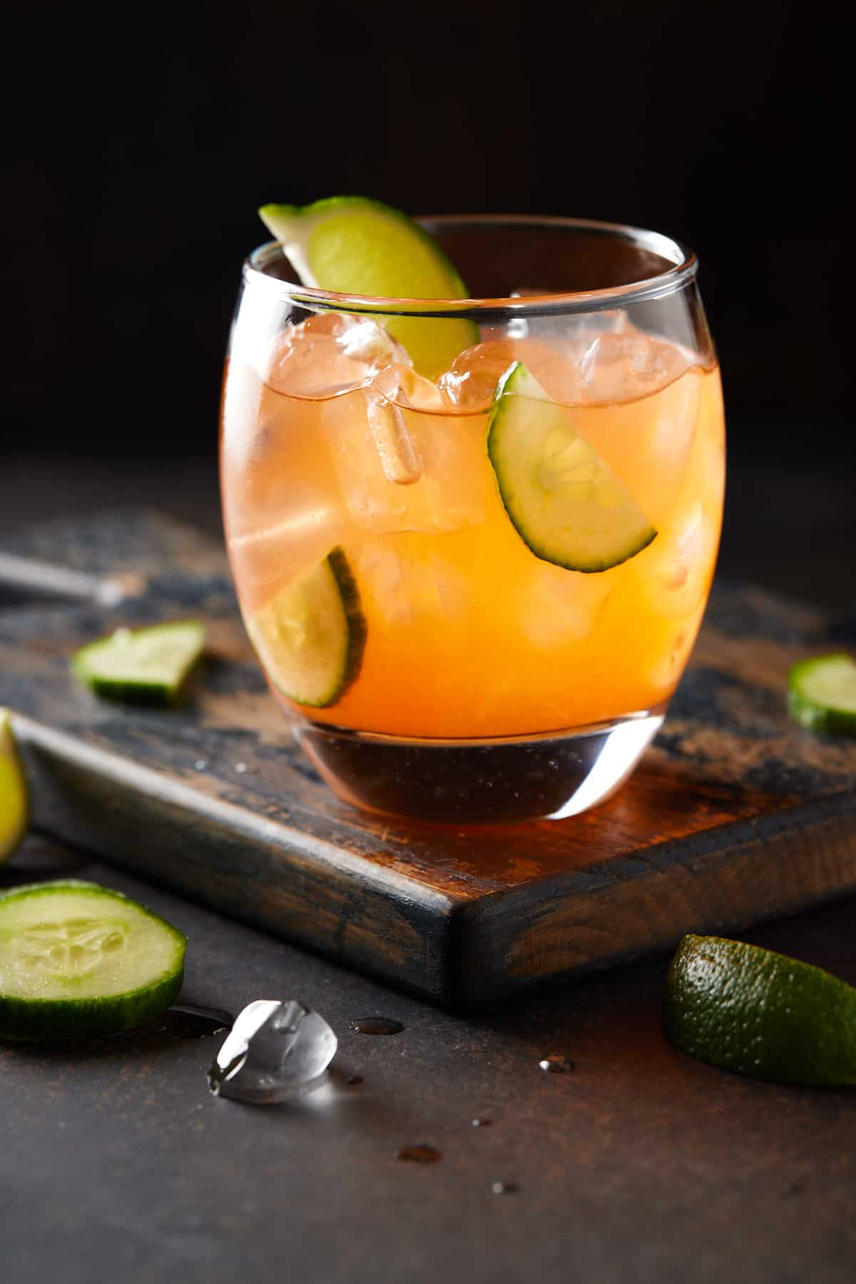 Aperol gin cocktail in low ball glass with limes and cucumber.