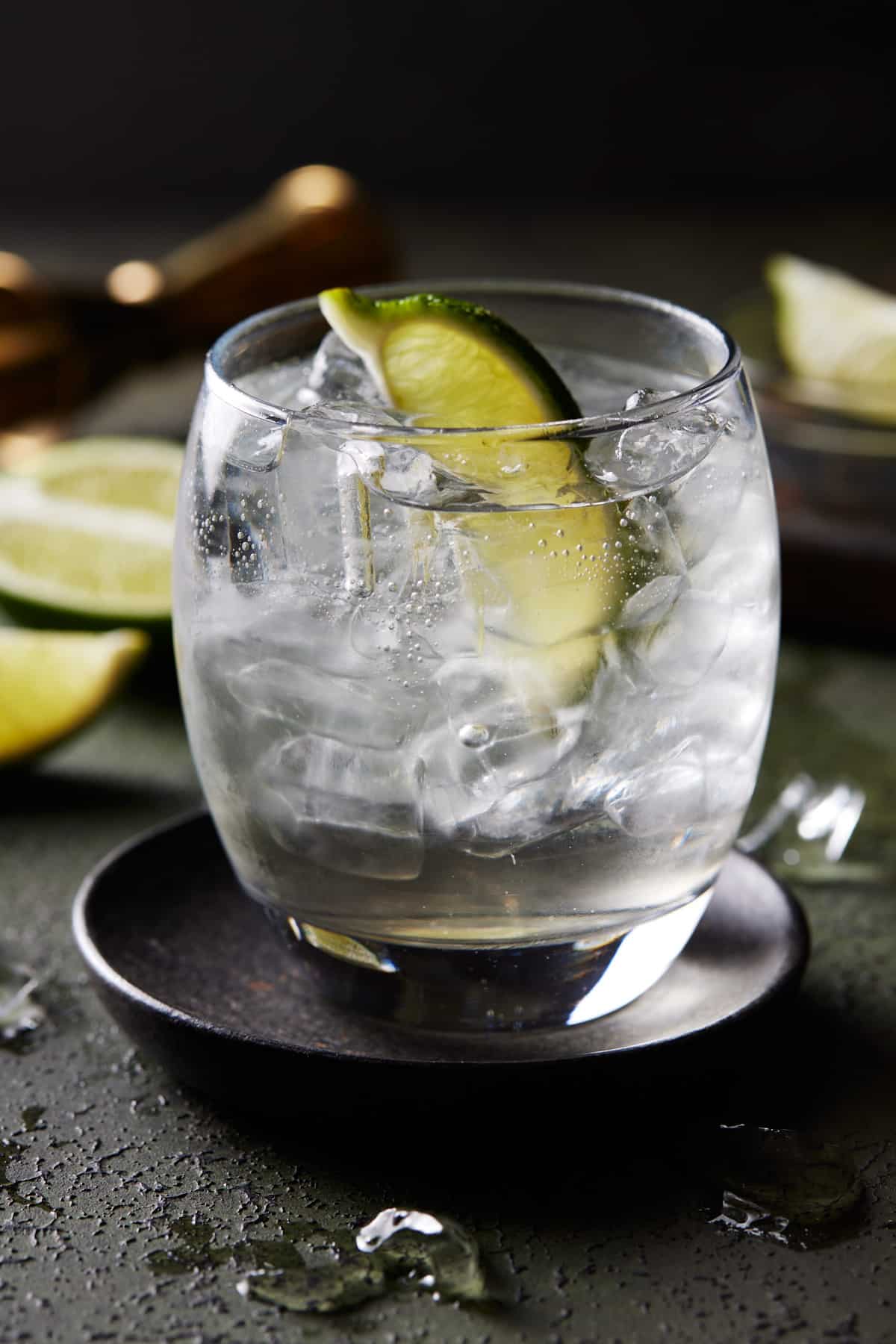 Elderflower Gin and Tonic in lowball glass filled with ice on black coaster. 